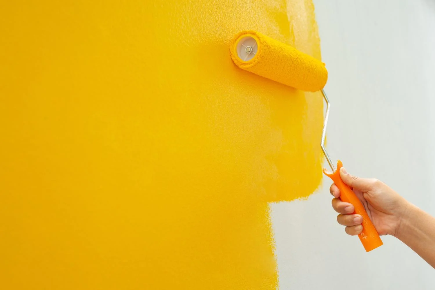 Gelbe Farbe wird mit einer Rolle auf eine Wand aufgetragen